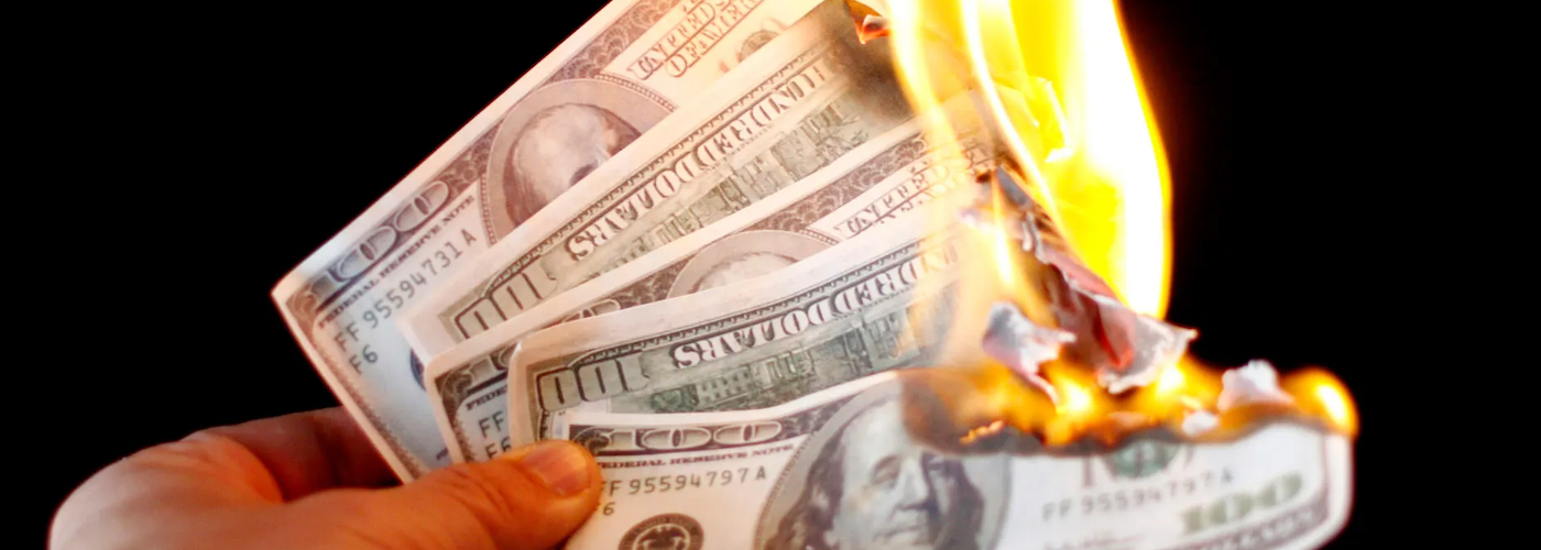A picture of a hand holding a set of five hundred dollar bills that have been lit on fire.